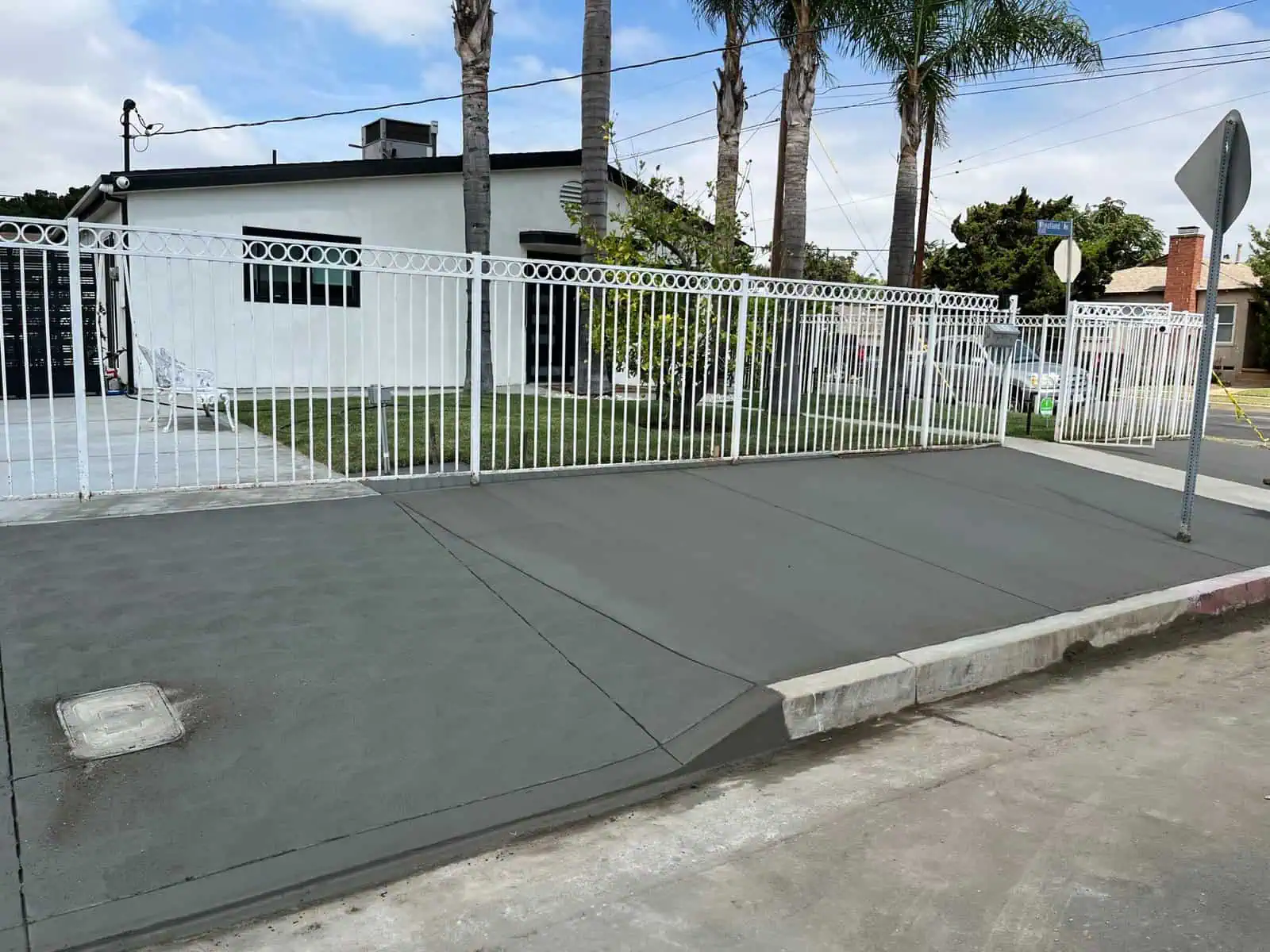 Newly poured concrete sidewalk with white metal fence in residential area.