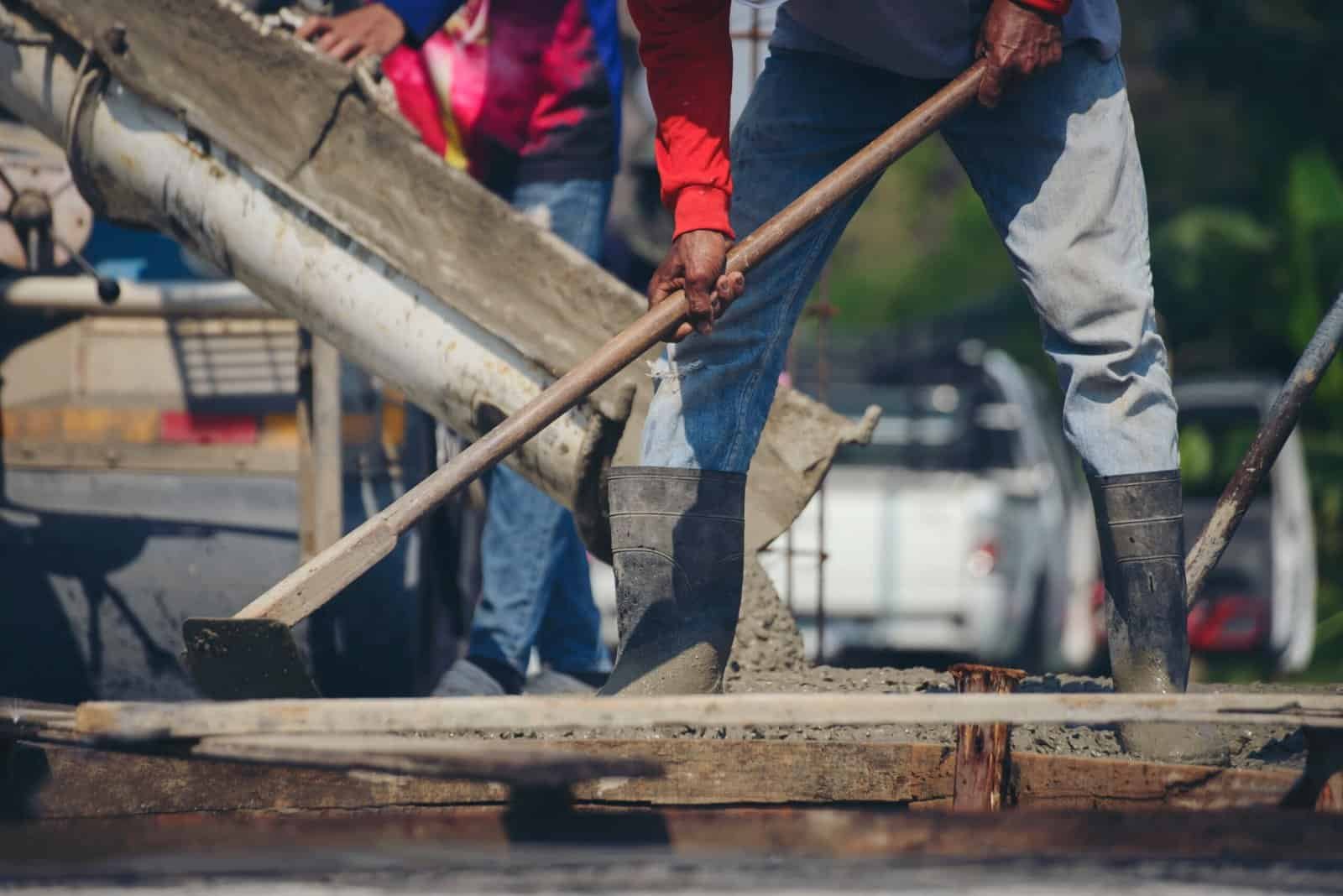 Workers pouring and leveling concrete at construction site.