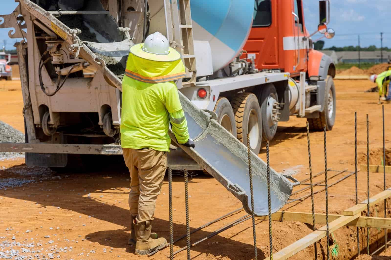 Worker pouring concrete from mixer truck at construction site.