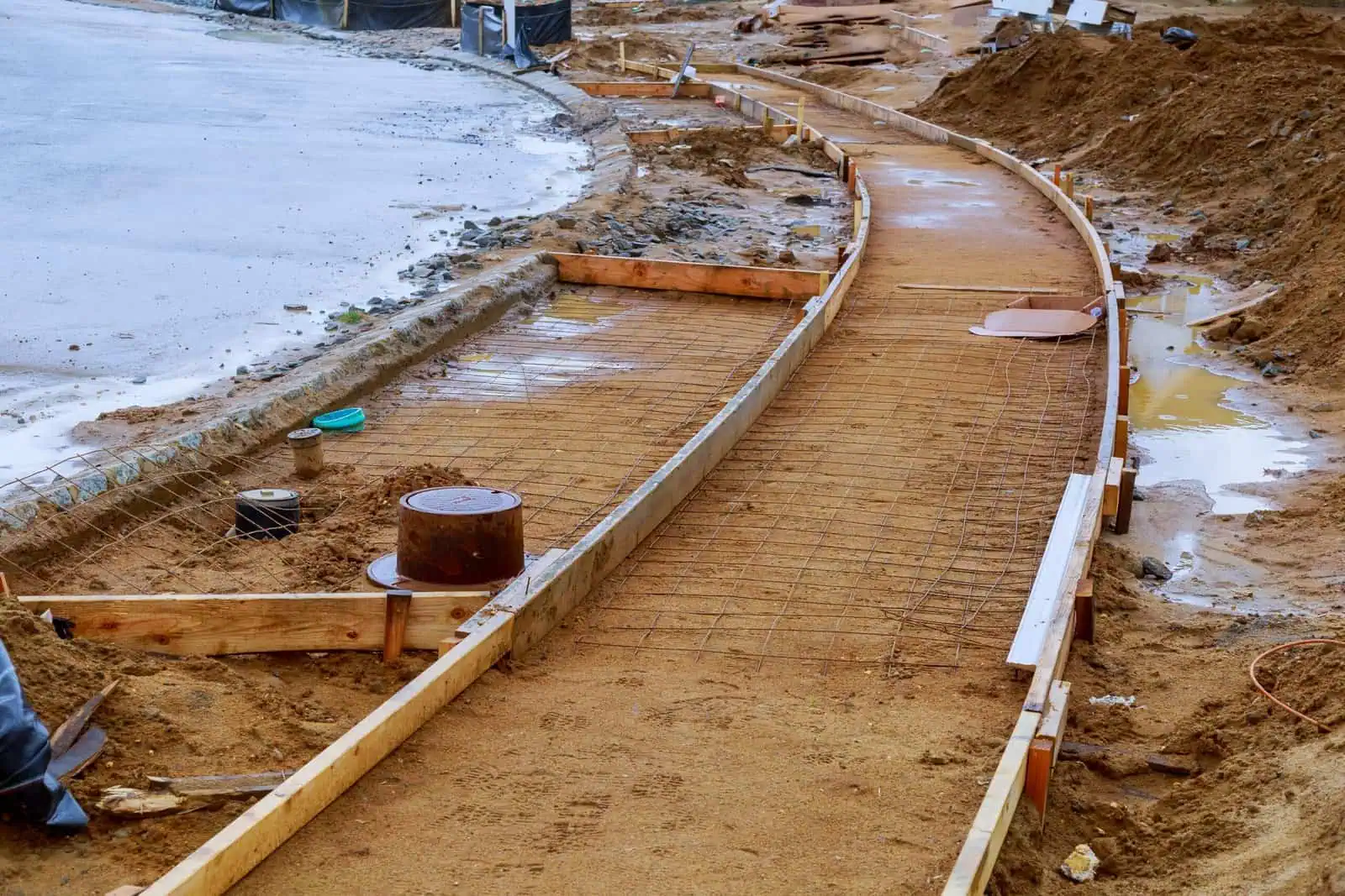 Curved concrete curb being built on a construction site with wooden forms and wet concrete.