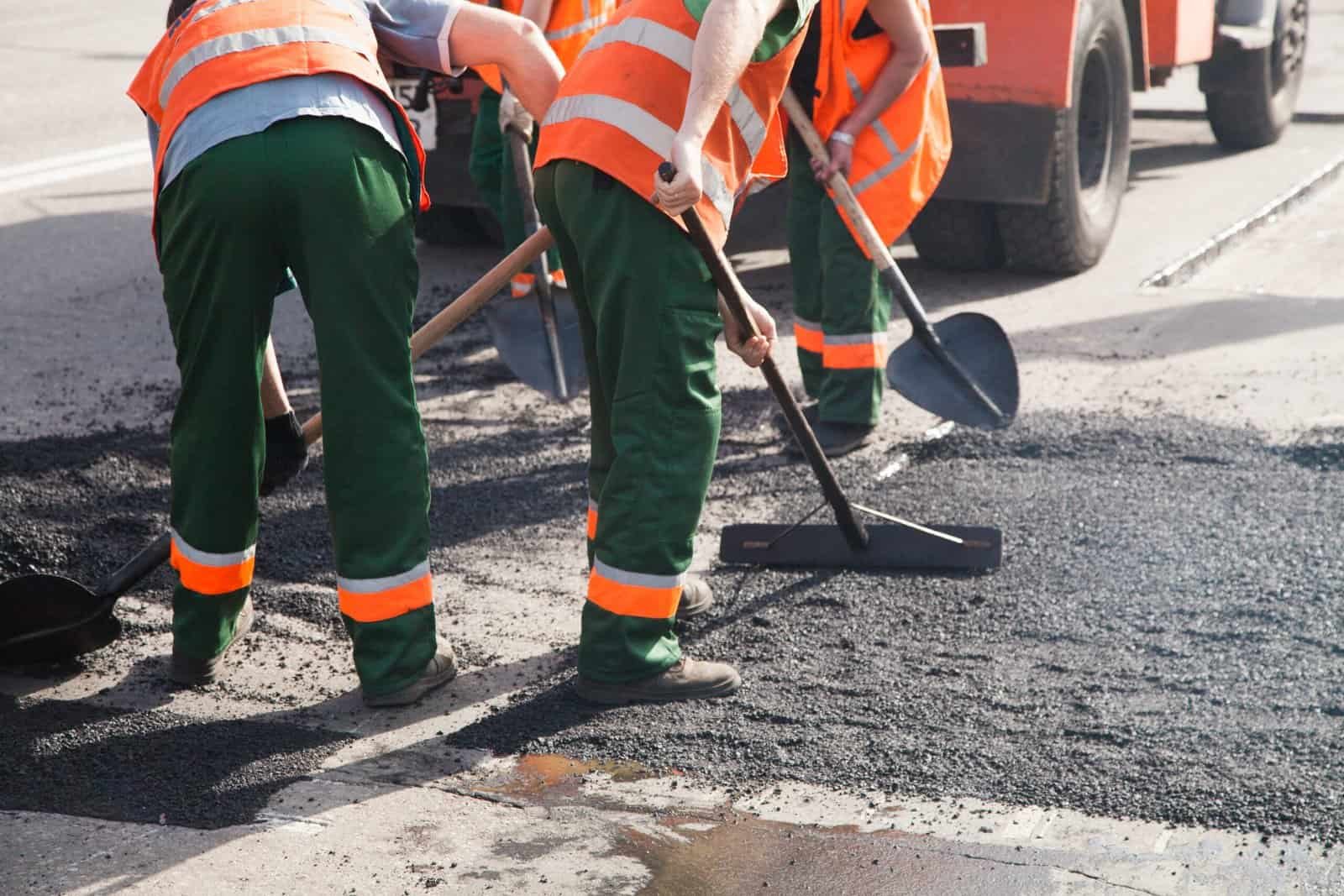 Workers repairing asphalt road with shovels and equipment.